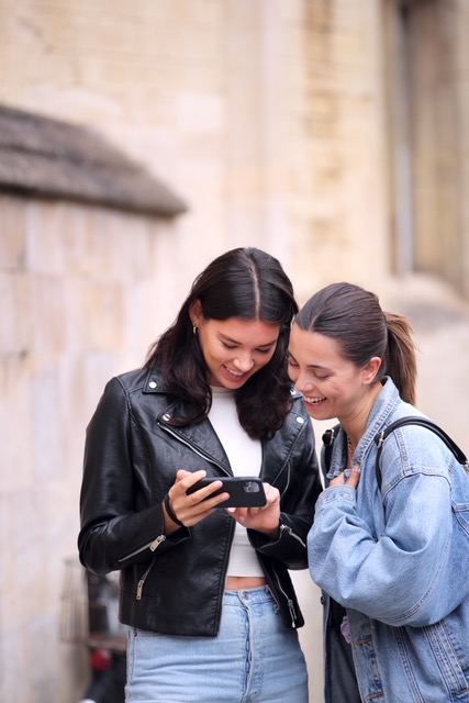 Same Sex Female Couple Sightseeing Looking At Mobile Phone And Walk Around Oxford UK Together